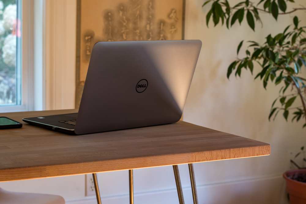 Dell laptop on a wooden office desk with a plant in the background